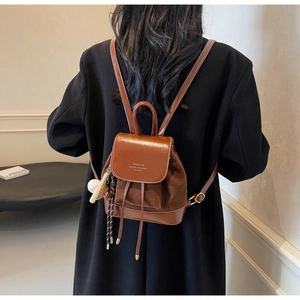 Detail of a brown mini backpack with leather and suede mix and a baseball charm