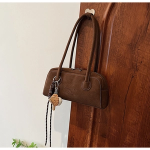Detail of a dark brown suede Boston bag featuring embossed text and a baseball glove charm