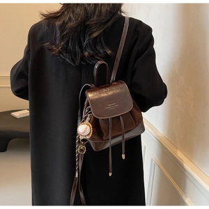 Detail of dark brown mini backpack with suede texture and creative baseball pendant charm