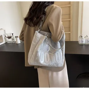 Sac fourre-tout argenté froissé avec chaîne en métal porté par un mannequin dans un café
