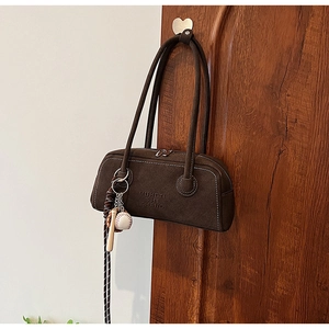 Detail of a dark brown suede underarm bag with a decorative baseball theme keychain