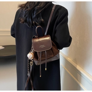 Detail view of small brown vintage leather backpack with drawstring and baseball charm