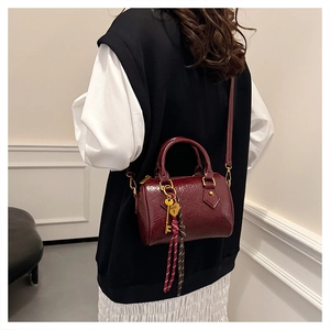 Detail view of burgundy Boston bag with cracked leather texture and golden pendant