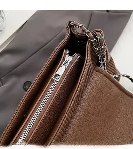 Gros plan sur la fermeture éclair en métal argenté et la bandoulière de ce sac marron