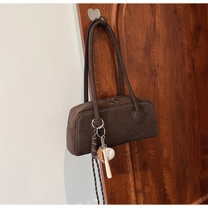 Detail view of brown suede underarm bag with MUHETI lettering and baseball charm