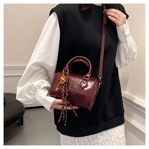 Detail of burgundy glossy Boston bag with braided rope and golden key charm