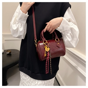 Close-up of wine red patent leather Boston bag featuring gold hardware and heart charm