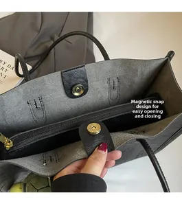 Detail of the magnetic snap closure and gray suede interior of a black tote bag