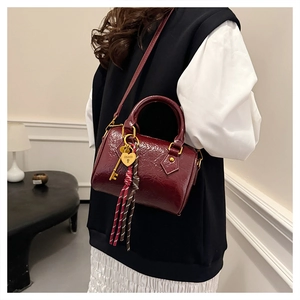 Detail of wine red glossy leather Boston bag featuring heart charm and gold hardware