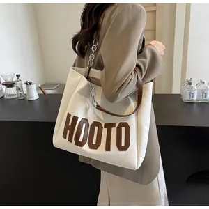 Vue détaillée d'un grand sac cabas en cuir blanc avec chaîne en métal et logo HOOTO
