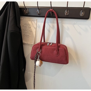 Detail of red suede-textured underarm bag featuring embossed logo and baseball charm accessory