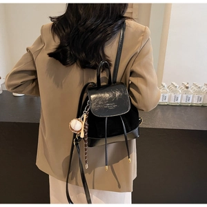 Detail of black mini backpack with drawstring closure and stylish baseball pendant