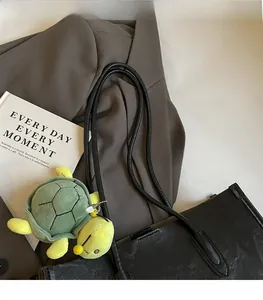 Detail of black pebbled leather tote bag with long straps and a green turtle plush charm