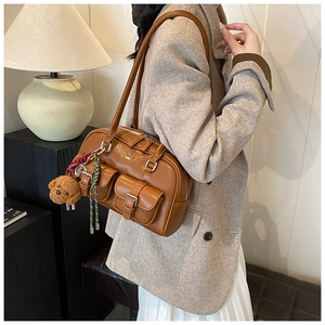 Detail view of brown vintage leather bowling bag with front pockets and plush bear charm