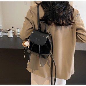 Close-up of black glossy leather backpack with creative baseball charm and gold hardware