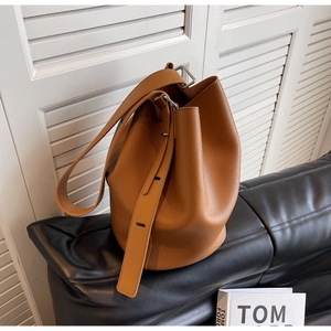 Detail of a brown bucket bag with lychee grain texture and wide shoulder strap