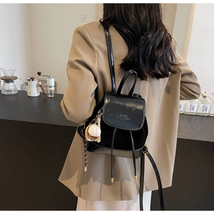 Close-up of stylish black mini backpack with mixed textures and baseball keychain