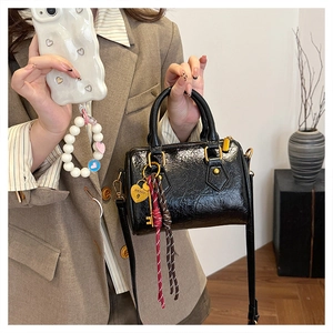 Detailed close-up of glossy black Boston bag with gold heart pendant and woven strap detail