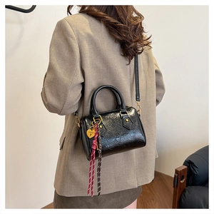 Detail of black glossy crinkled mini Boston bag featuring gold hardware and heart charm