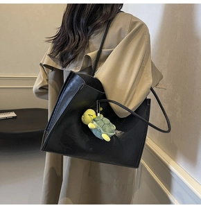 Minimalist black tote bag shown on shoulder with green turtle plush keychain