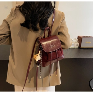 Detail of burgundy leather mini backpack with metal handle and decorative sport pendant