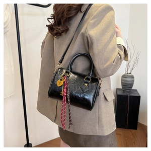 Detail view of black glossy Boston bag with golden heart charm and woven ribbon strap