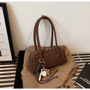 Detail of a brown suede shoulder bag with baseball charms on a beige trench coat