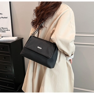 Détail d'un sac cabas noir matelassé avec plaque argentée et bandoulière chaîne sur modèle