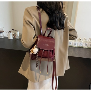 Detailed view of dark burgundy mini backpack with mixed leather texture and baseball charm