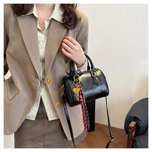 Detail of black patent leather Boston bag featuring heart charm and braided rope accent