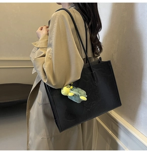 Close-up of black retro leather tote bag with a green plush turtle charm accessory