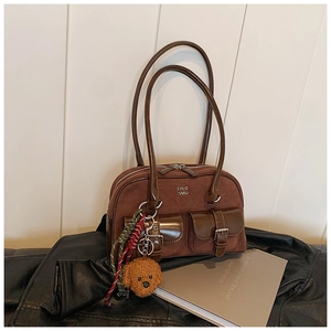 Close-up of brown suede bowling bag with leather straps and teddy bear charm on leather jacket