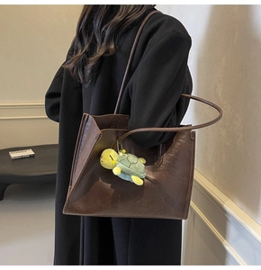 Detail of dark brown leather tote bag with long straps and a turtle charm on a model