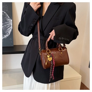 Detail of brown Boston bag with golden heart pendant and pleated leather texture on model