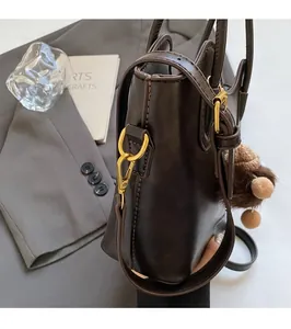Dettaglio borsa a secchiello marrone con finiture dorate lucide e ciondolo di peluche