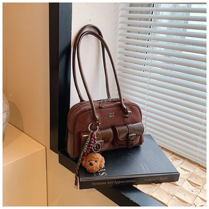Detailed macro view of vintage brown suede shoulder bag with dual buckles and plush bear charm