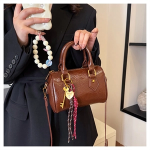 Close-up of brown glossy Boston bag with golden key pendant and braided strap details