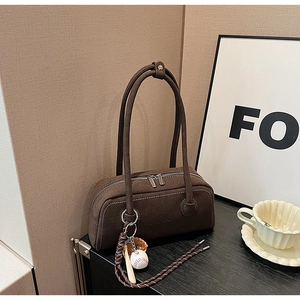 Close-up of deep brown matte shoulder bag with silver double zippers and baseball charm