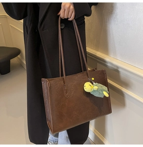 Detail of dark brown leather tote bag with vintage texture and green turtle pendant