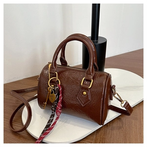 Close-up of chocolate brown Boston bag with golden heart charm and woven tassel detail