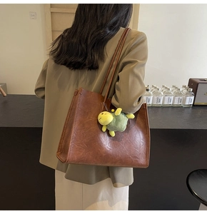 Brown leather tote bag detail with cute green plush turtle charm in a stylish setting