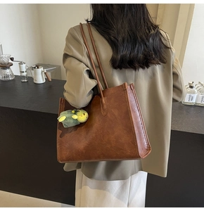 Detail view of large brown vintage tote bag with a small green plush turtle charm