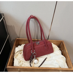 Close-up of red suede underarm bag with letter embossing and baseball charm on wood