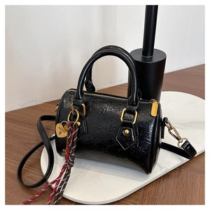 Close-up of black glossy leather Boston bag with gold hardware and heart pendant charm