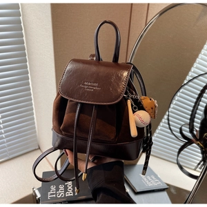 Detail view of brown faux leather mini backpack featuring tassel cord and baseball charm