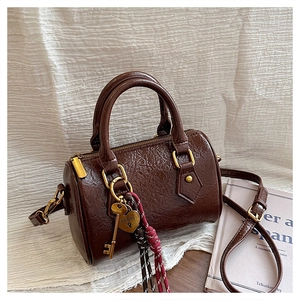 Detail of a brown Boston bag showing pleated faux leather texture and gold heart lock charm