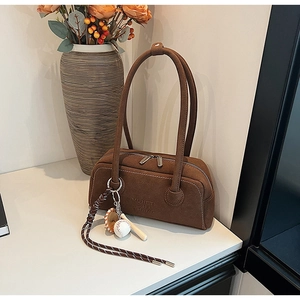 Detail of vintage brown suede shoulder bag with dual zippers and decorative baseball charm