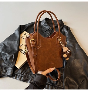 Dettaglio borsa a secchiello vintage in pelle marrone con ciondolo e testo inciso