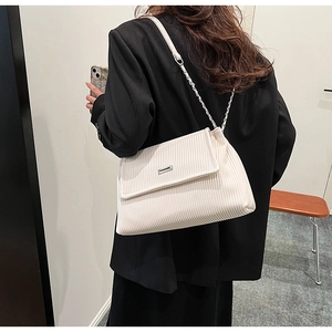 Détail du sac plissé crème porté à l'épaule avec chaîne argentée et fermoir métal