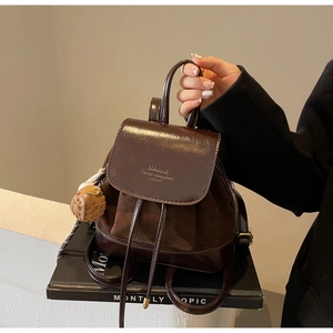 Detail of a brown vintage backpack featuring suede stitching and a cute bear charm